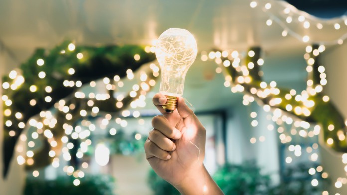 A hand holding a glwoing light bulb